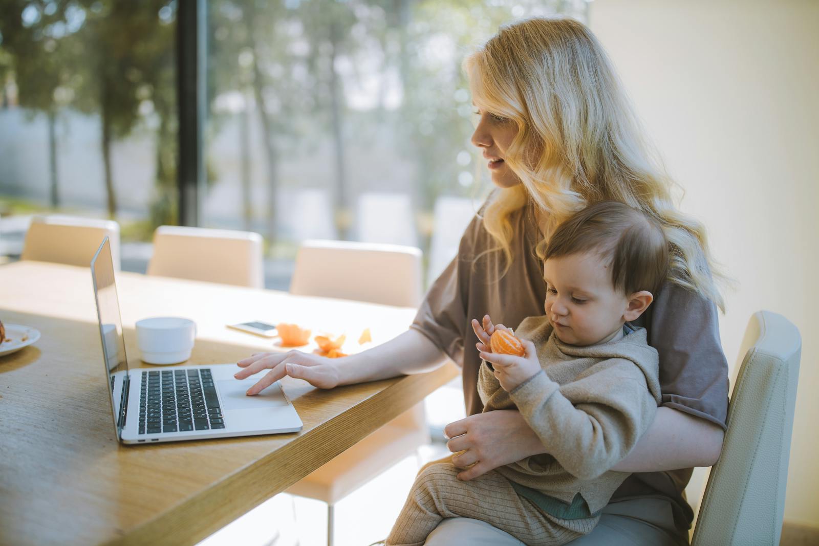 Woman Carrying her Baby and Working on a Laptop